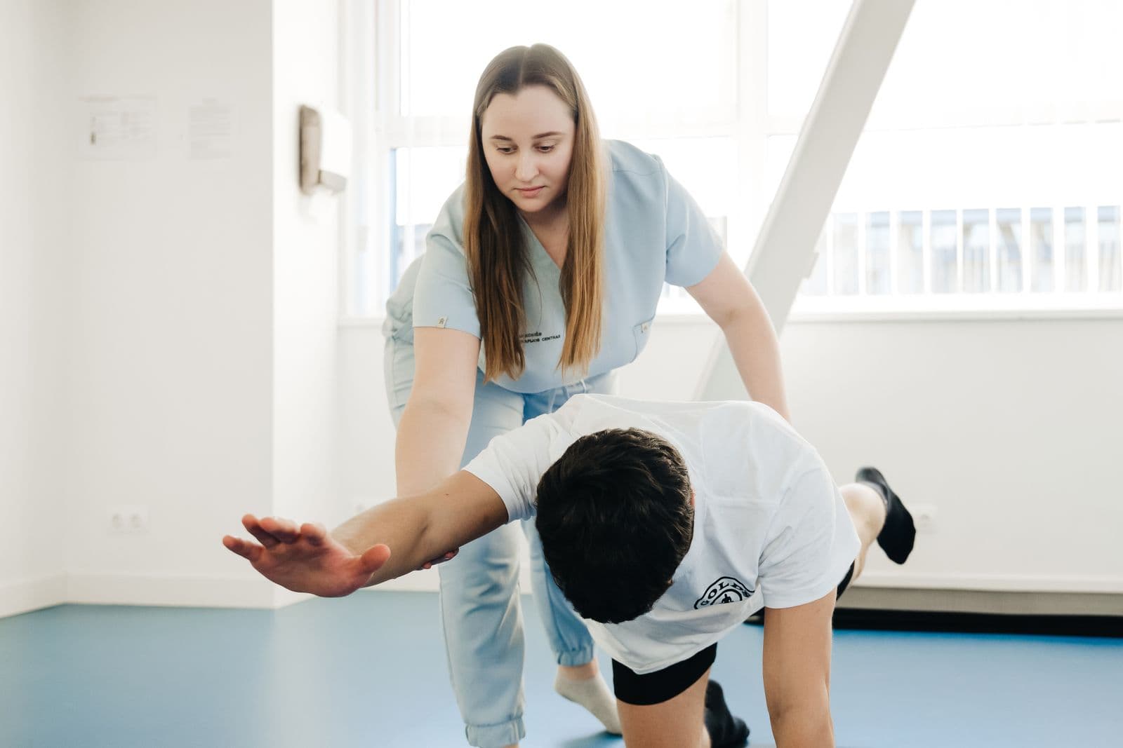 Behandler hjælper en patient med en strækøvelse på gulvet i en lys klinik
